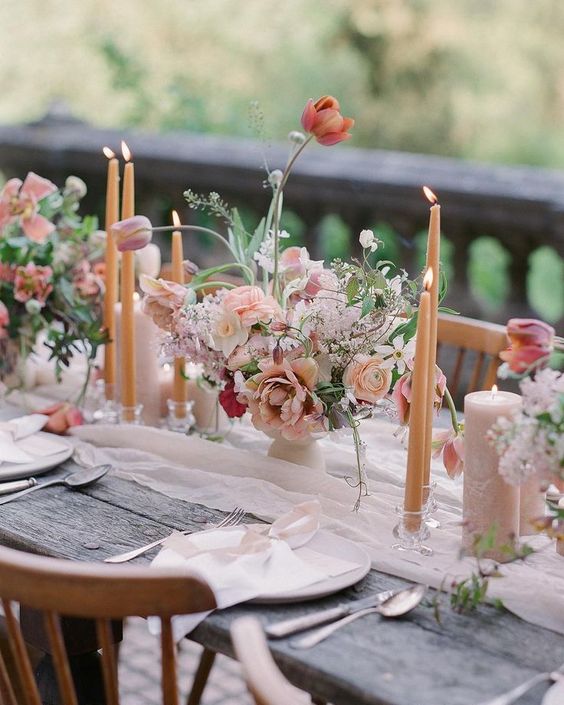 a blush wedding tablescape with candles, blooms, greenery, white porcelain, white linens and silver cutlery is very romantic