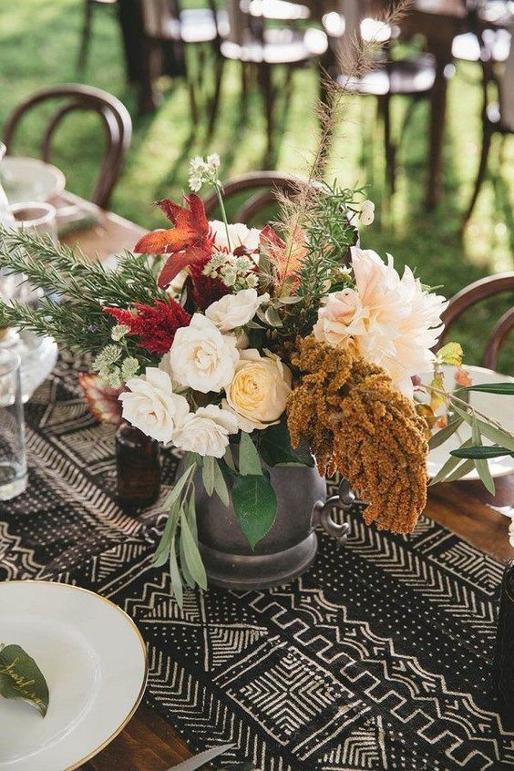 a boho wedding tablescape with a black and white printed runner, white and burgundy blooms, gold-rimmed plates