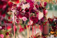 a bold and lush wedding centerpiece of blush, white and burgundy blooms and some leaves plus a matching table runner