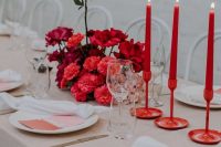 a bold and modern Valentine’s Day wedding table with red candles in matching candleholders, a bold red and fuchsia floral arrangement, a blush tablecloth, silver cutlery