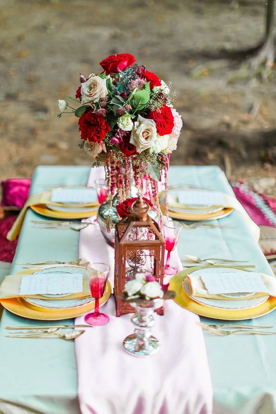 a bright and bold Valentine's Day wedding table with bold blooms, a candle lantern, gold chargers and colorful glasses