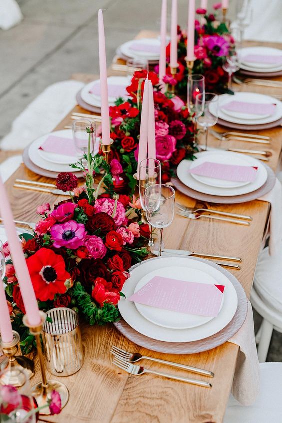 a bright and chic Valentine's Day wedding table with red, fuchsia, burgundy blooms, blush candles and menus, gold cutlery and gold candleholders