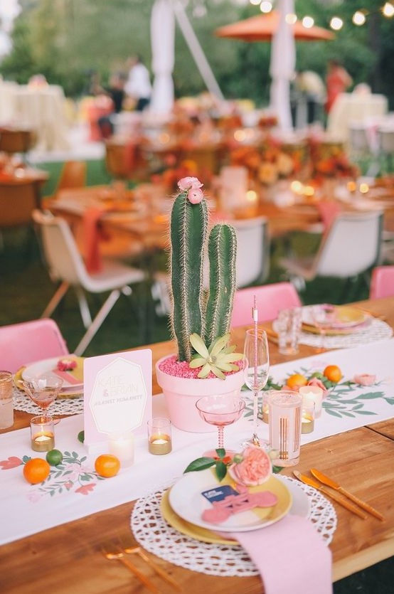a bright and fun summer wedding tablescape with a printed runner, pink linens, candles and glasses, potted cacti