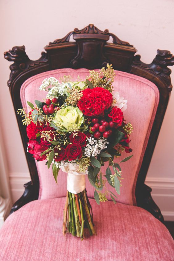 a bright red and white wedding bouquet of greenery, blooms, berries and with a white ribbon wrap for a Valentine bride