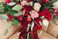 a bright red, white and pink rose wedding bouquet with greenery and blush and burgundy ribbons is amazing