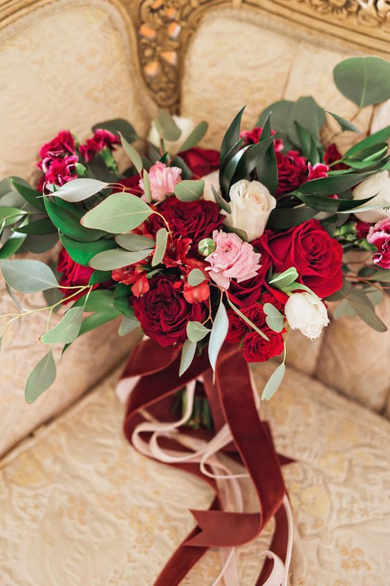 a bright red, white and pink rose wedding bouquet with greenery and blush and burgundy ribbons is amazing
