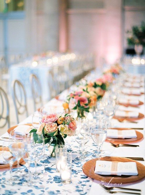 a chic and cool wedding tablescape with a blue printed table runner, pink blooms and greenery and smoked glass chargers plus neutral napkins