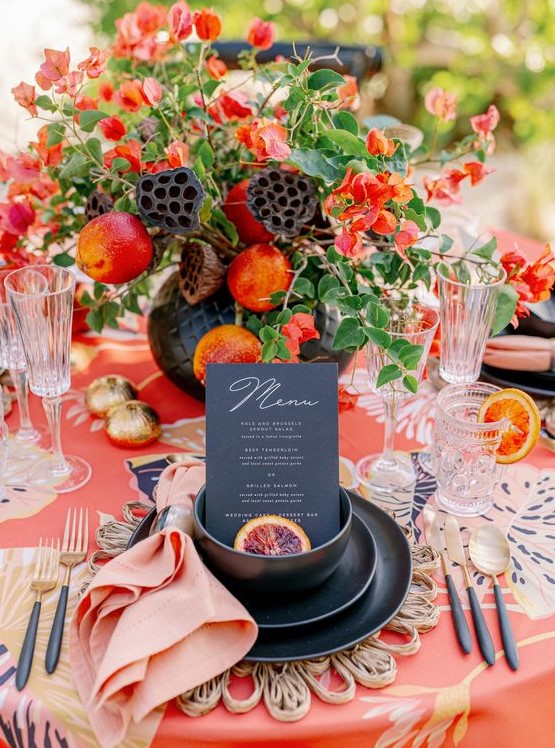 a colorful dramatic summer wedding table with a printed tablecloth, a super bold floral centerpiece with fruits, gold porcelain and cutlery