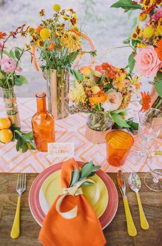 a colorful summer wedding tablescape with a printed table runner, bright blooms, glasses and neon cutlery, colorful plates