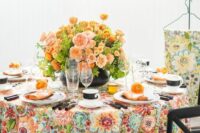 a colorful wedding table setting with a bright floral tablecloth, bold blush and orange blooms, black cutlery and mugs
