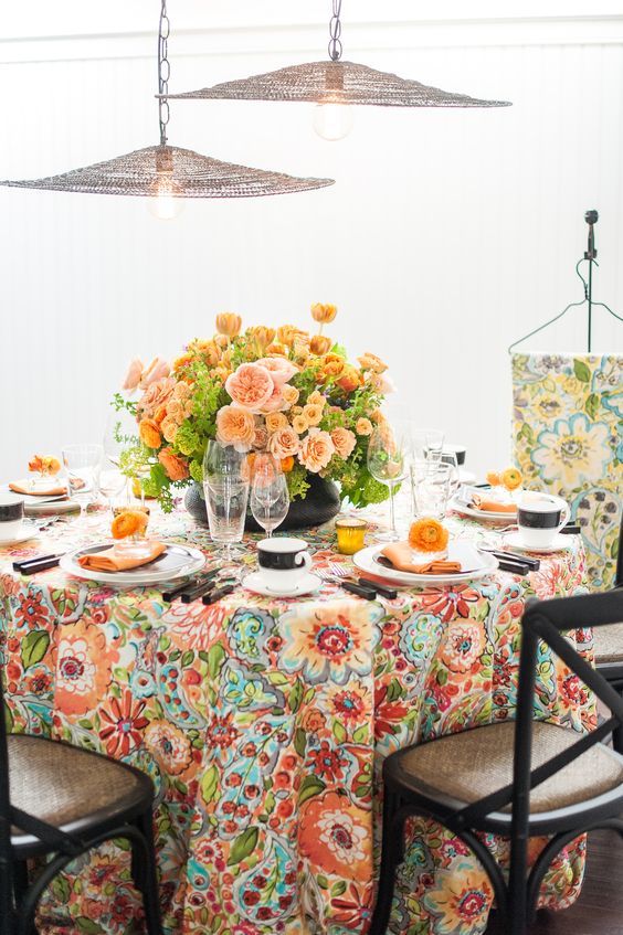 a colorful wedding table setting with a bright floral tablecloth, bold blush and orange blooms, black cutlery and mugs