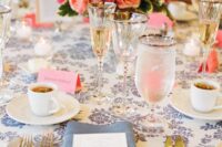 a colorful wedding tablescape with a navy printed tablecloth, super bright blooms and greenery, a blue napkin and gold-rimmed glasses