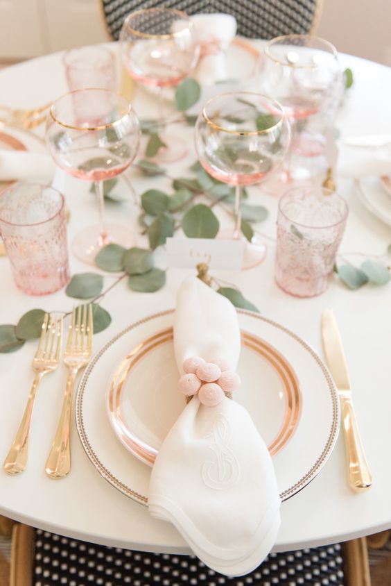 a cute and airy Valentine's Day wedding table with blush glasses, gold rimmed glasses, silver cutlery and greenery on the table
