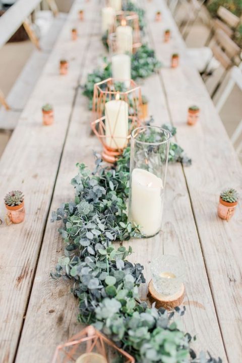 a cute greenery and foliage table runner with candles and copper canlde holders for a fresh wedding reception