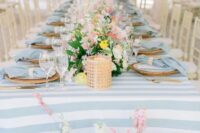 a delicate pastel wedding tablescape with a blue striped tablecloth, pastel blooms, blue napkins and candleholders
