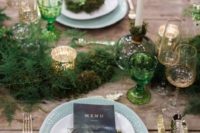 a fern table runner, tall candles and green glasses and mercury glass candle holders on an uncovered table