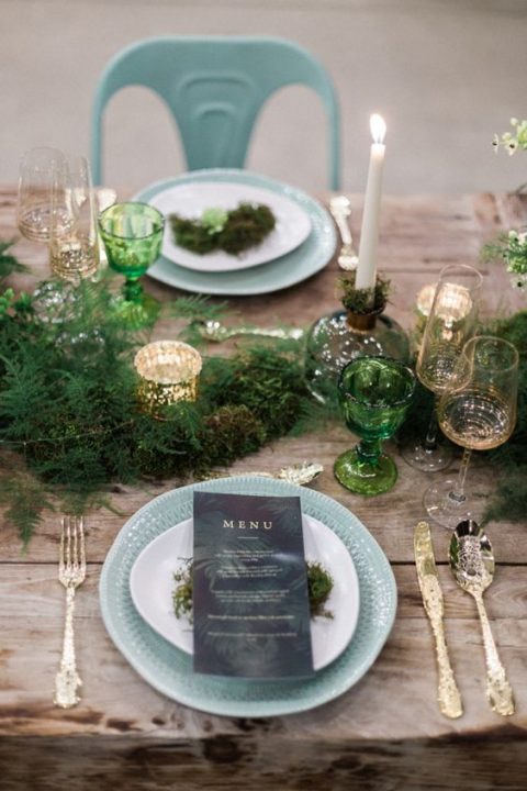 a fern table runner, tall candles and green glasses and mercury glass candle holders on an uncovered table