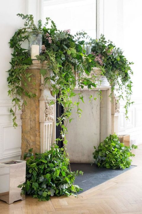 a fireplace decorated with lush and textural greenery and candles can be a nice ceremony space