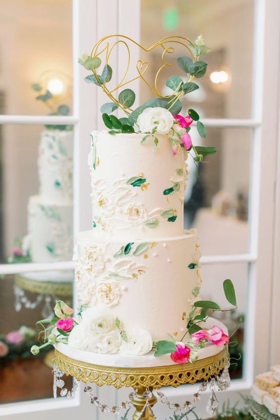 a fresh spring wedding cake with white sugar blooms and leaves painted, with gold foil and fresh greenery and blooms on top