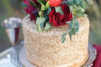 a gold Valentine wedding cake topped with red and burgundy blooms and greenery is amazing