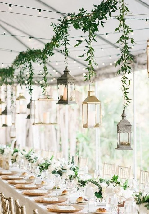 a greenery garland with lanterns hanging on it as a reception decoration and greenery and white bloom centerpieces match this decor