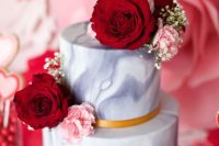 a grey marble wedding cake with gold ribbons, red and pink blooms and a red heart topper is adorable