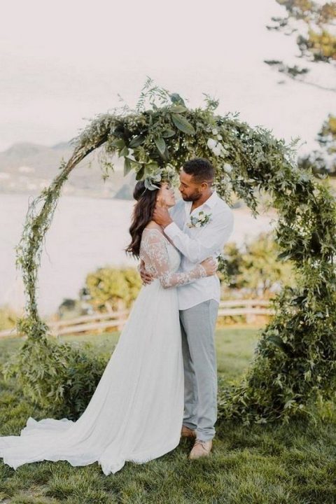 a large circular wedding arch covered with textural greenery is a fresh and bright idea for your wedding