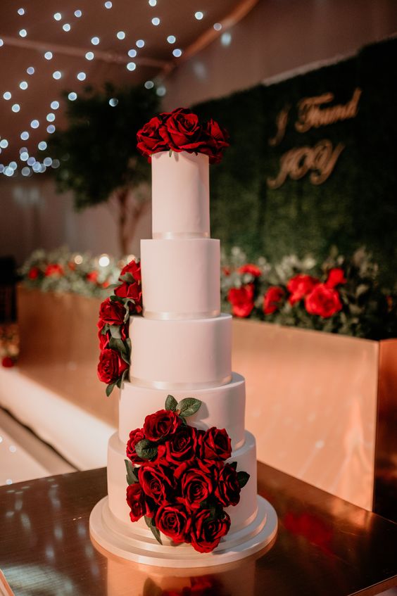 a large white wedding cake decorated with red roses is all about traditional elegance and chic and will fit a Valentine wedding