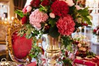 a lavish Valentine’s Day wedding table with burgundy and fuchsia linens, a bold red and pink floral arrangement, cages with blooms