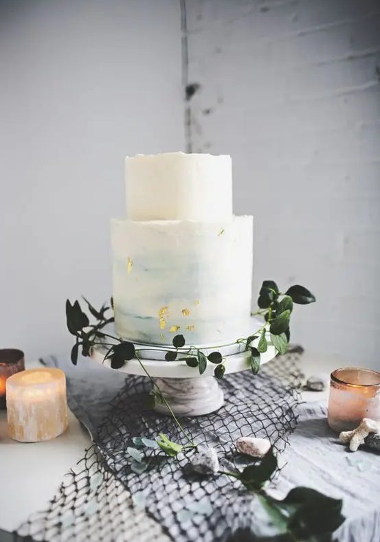 a light blue watercolor wedding cake with a rough edge, gold flakes and some greenery around
