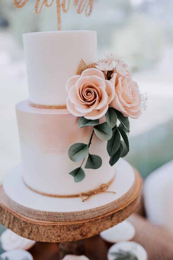 a lovely ombre blush wedding cake with pink and white sugar blooms, faux greenery and a glitter cake topper will do for a spring or summer wedding