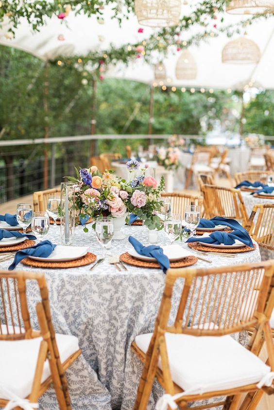 a lovely wedding tablescape with a grey printed tablecloth, navy napkins, woven placemats, pastel blooms and greenery is cool