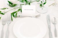 a minimalist and airy tablescape in white, with candles and a touch of fresh greenery