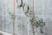 a minimalist wedding arch of copper, with greenery and copper hoops hanging from it