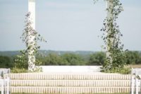 a minimalist white wedding arch decorated with lush foliage is a stylish idea