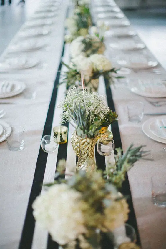 a modern wedding tablescape with a neutral tablecloth and a striped table runner, neutral blooms and candles, white plates
