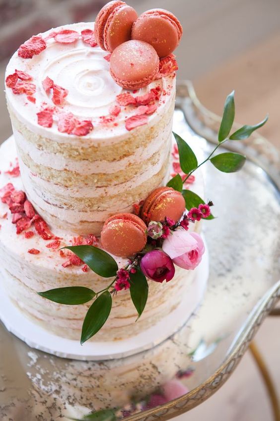 a naked wedding cake topped with bold coral petals and macarons, pink and purple blooms and greenery for a colorful spring wedding