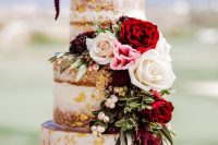 a naked wedding cake with gold leaf, pink, white and red blooms and greenery and some berries is fantastic