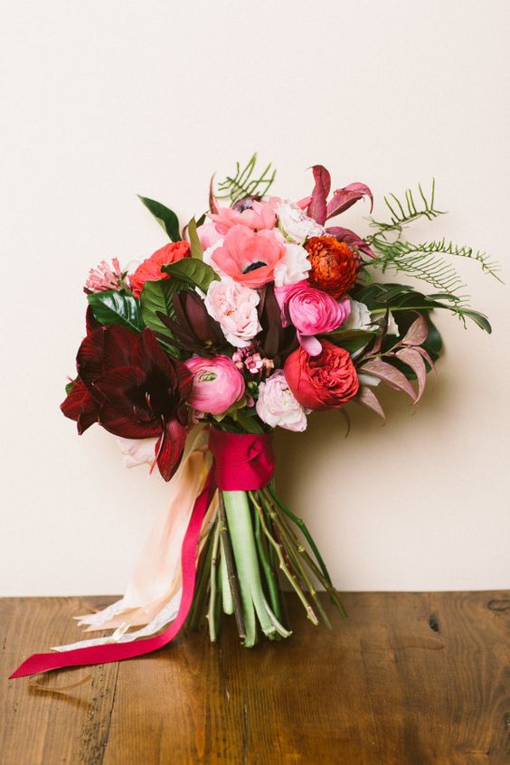 a pretty Valentine wedding bouquet of burgundy, pink, red and blush blooms and greenery and colorful ribbons