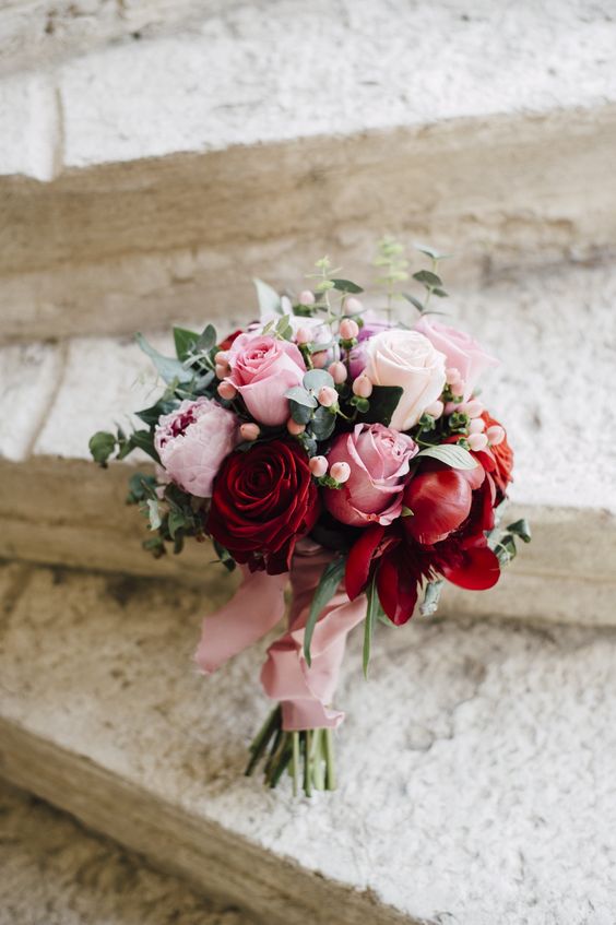 a pretty and cute Valentine wedding bouquet with pink and red peony and usual roses, berries and green and pink ribbons