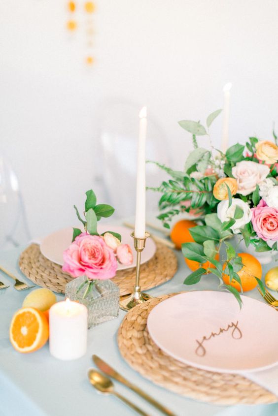 a pretty pastel Valentine's Day wedding table with woven chargers, blush plates, gold candleholders and calligraphy, candles and citrus