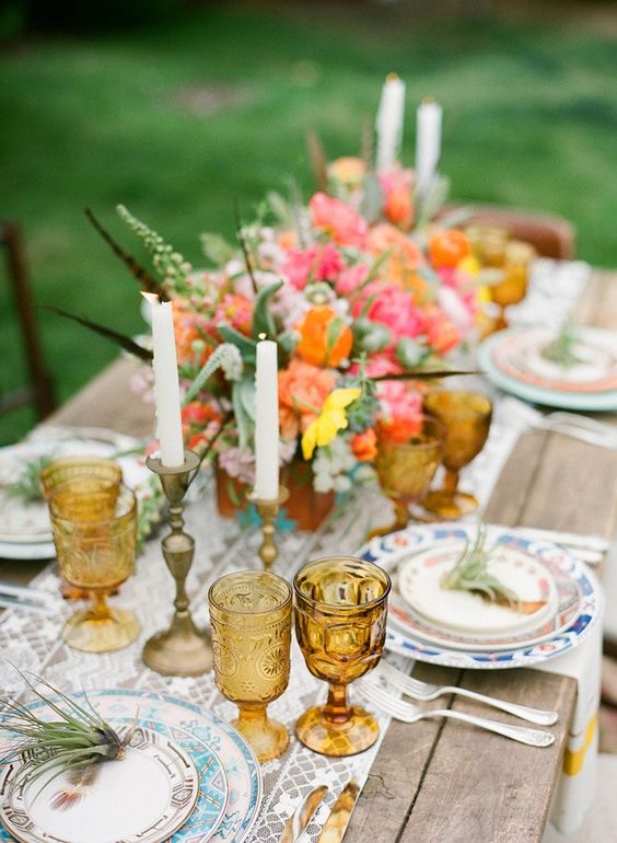 a quirky wedding tablescape with a printed table runner and plates, bright blooms and greenery, amber glasses and candles