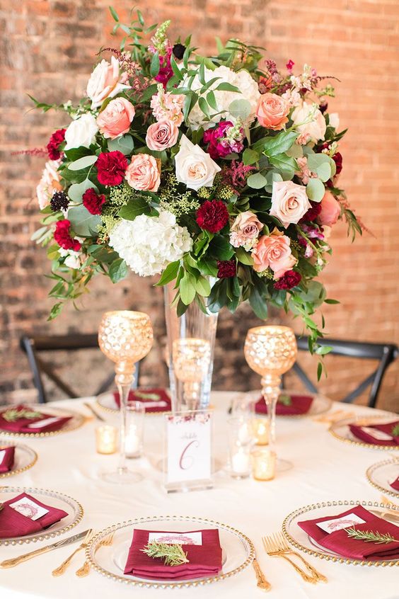a refined Valentine's Day wedding table with gold cutlery, gold rimmed chargers, a bold floral centerpiece and burgundy napkins