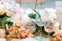 a refined and chic Valentine’s Day wedding table with peachy and pink blooms, a wooden placemat, candles and exquisite glasses