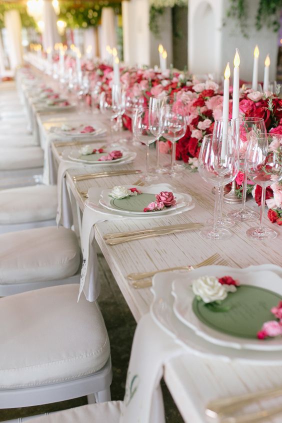a refined and romantic Valentine's Day wedding table with bold pink and red blooms, candles, refined plates and chic cutlery