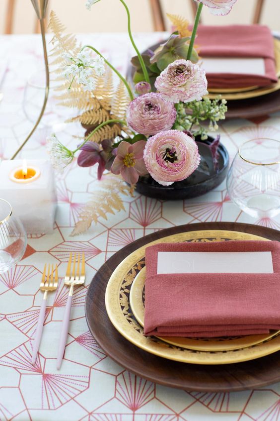 a refined modern wedding tablescape with a printed tablecloth, gold plates and red napkins, a chic ikeabana-style centerpiece