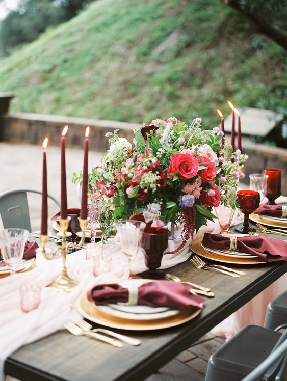 a romantic Valentine's Day wedding table with burgundy napkins, candles and golblets, a pink runner and a bold floral arrangement