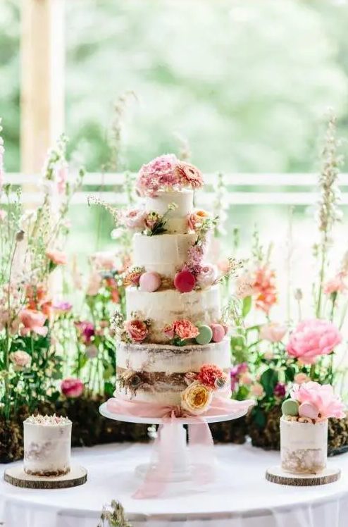 a romantic secret garden wedding cake - a naked one with bold blooms and colorful macarons plus pink ribbons is wow