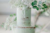 a semi-naked green wedding cake topped with white baby’s breath, eucalyptus and an acrylic topper for a modern boho wedding