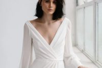 a simple minimalist wedding dress with a deep V-neckline, sleeves on buttons and a bit of drapery